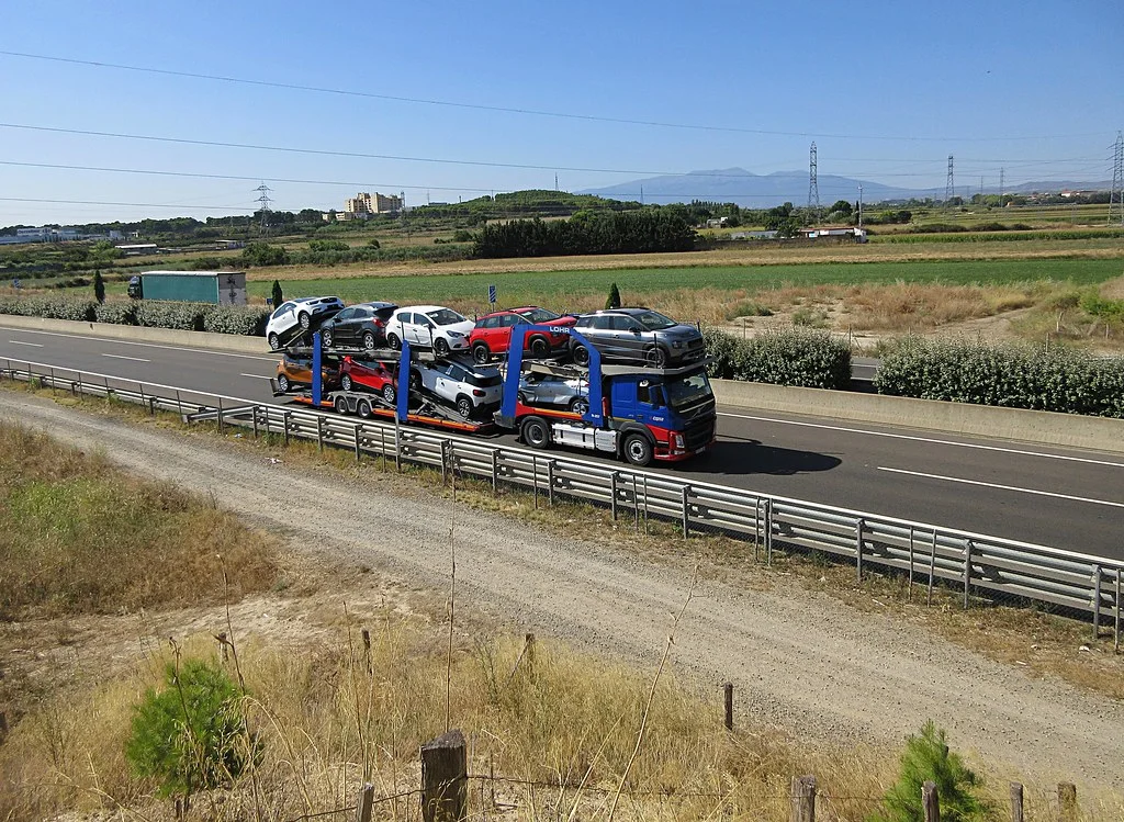 Góndola madrina portavehículos cargada con autos en dos niveles circulando por una autopista